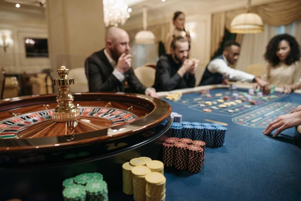 Men playing cards at a table with a roulette wheel and markers in front